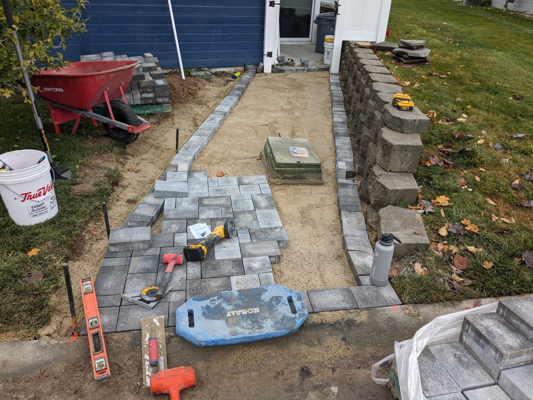 Paver walkway installation in progress beside a retaining wall
