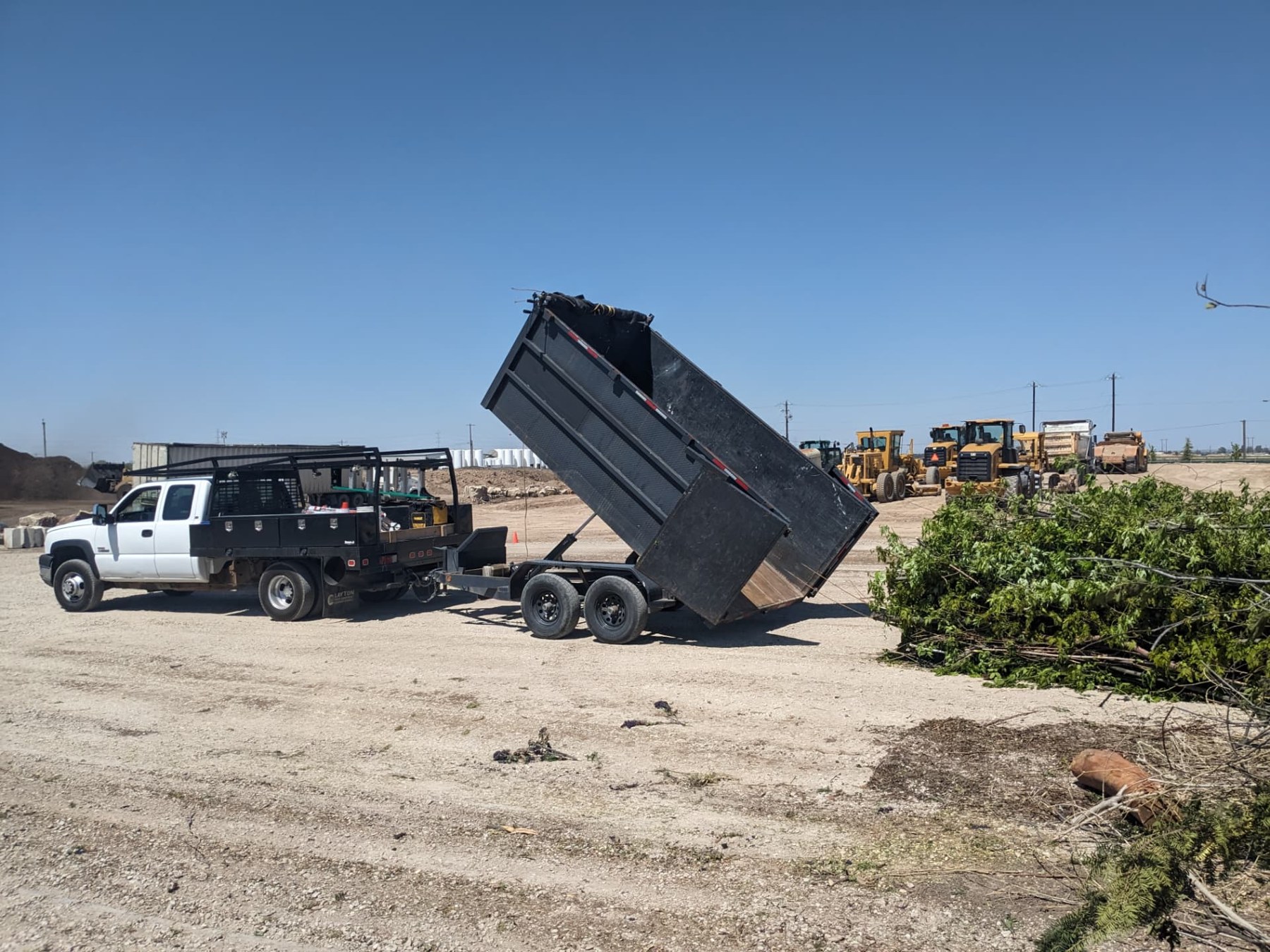 Truck and raised dump trailer unloading branches at a disposal site