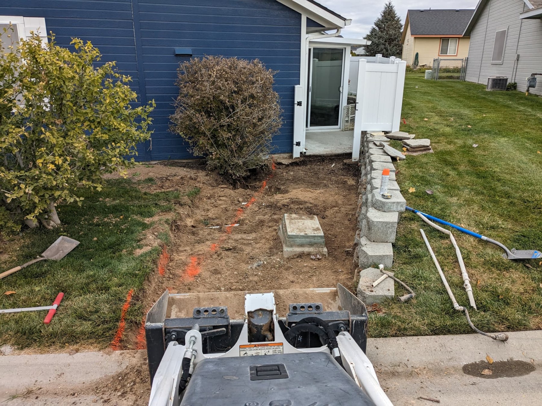 Compact loader preparing an entry walkway beside a retaining wall