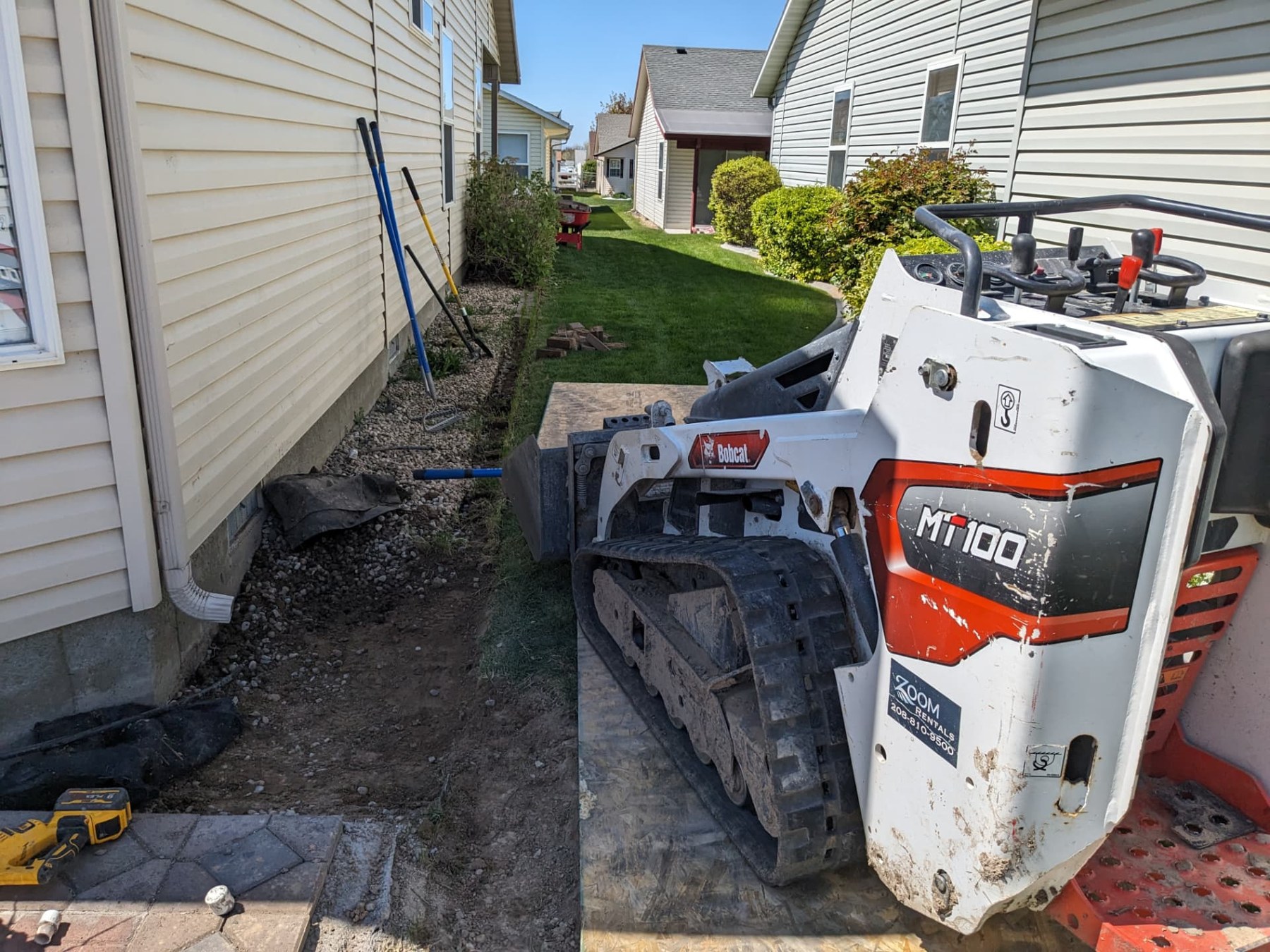 Compact loader working in a narrow side yard during landscaping