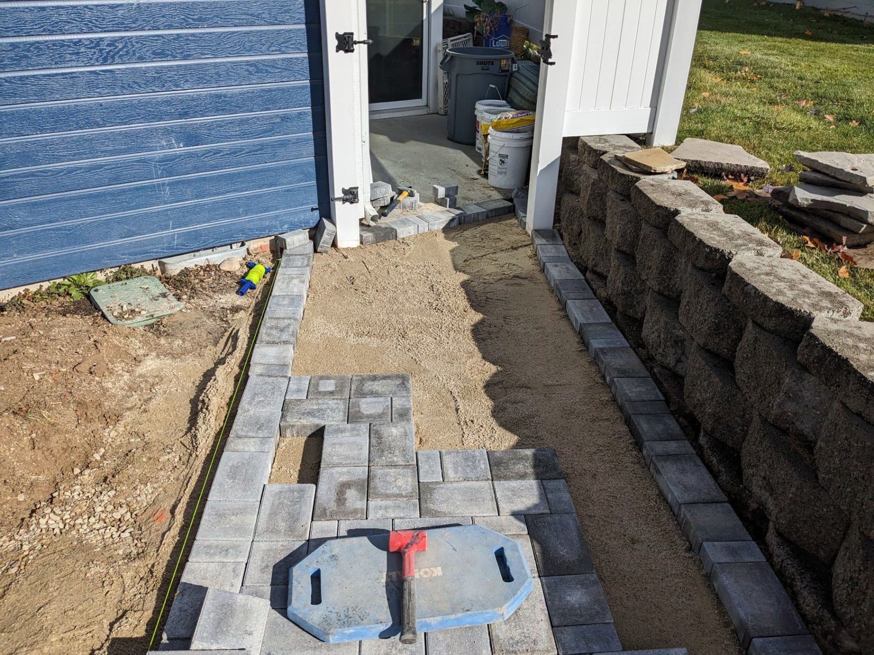 Gray pavers being installed beside a retaining wall and blue home