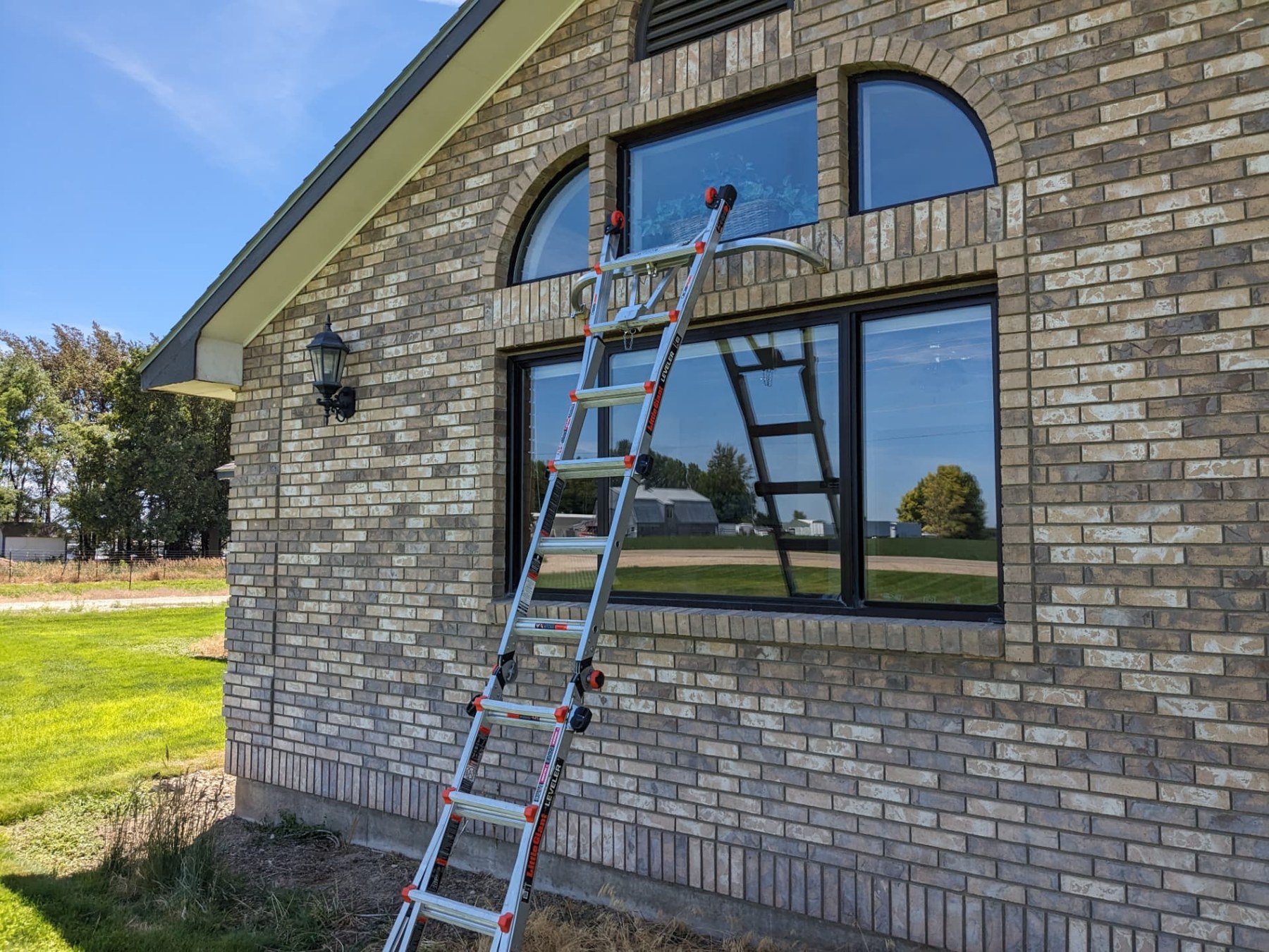 Ladder set up to clean tall exterior windows on a brick home