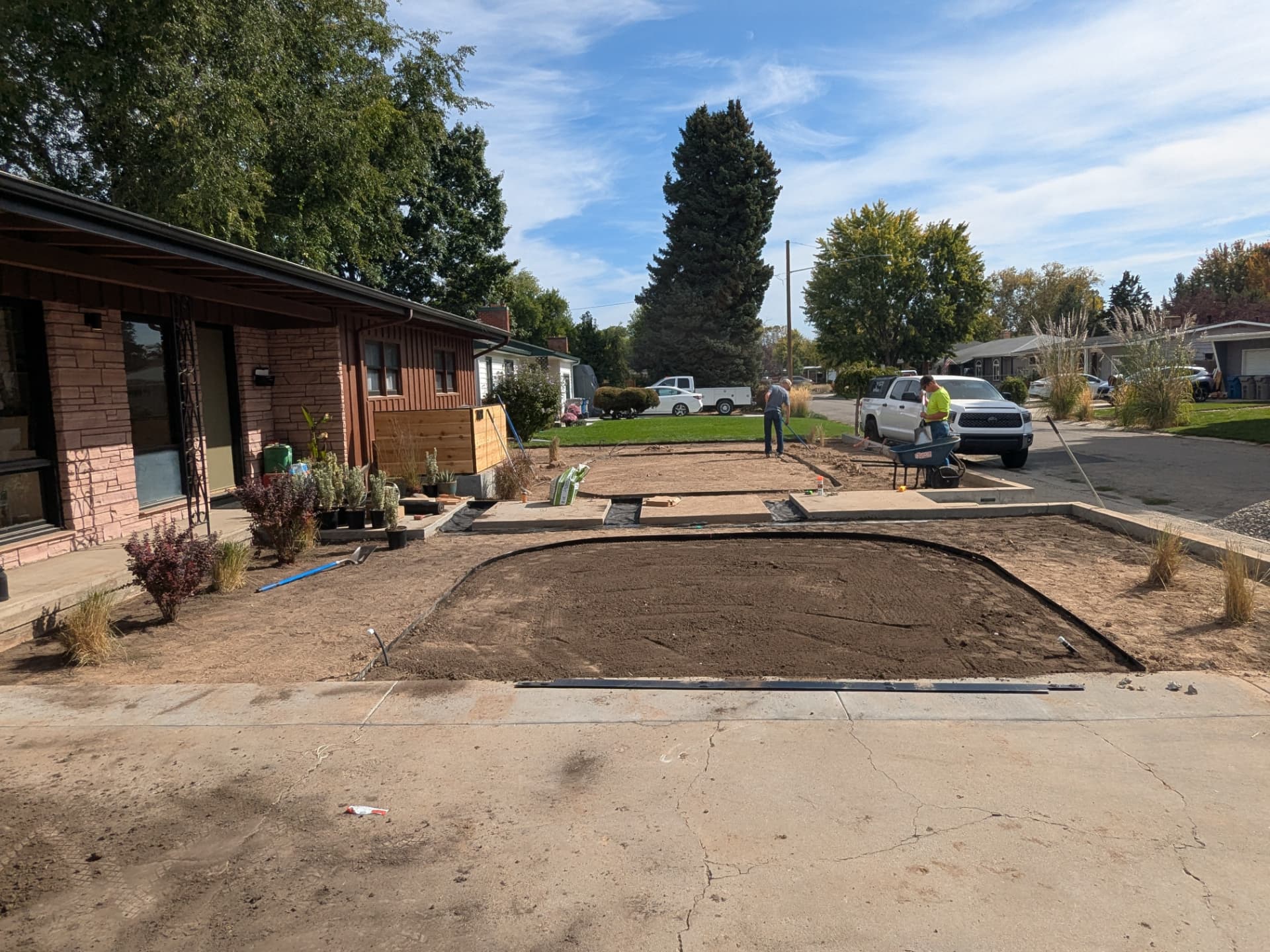Crew grading soil beds and installing edging in a residential front yard
