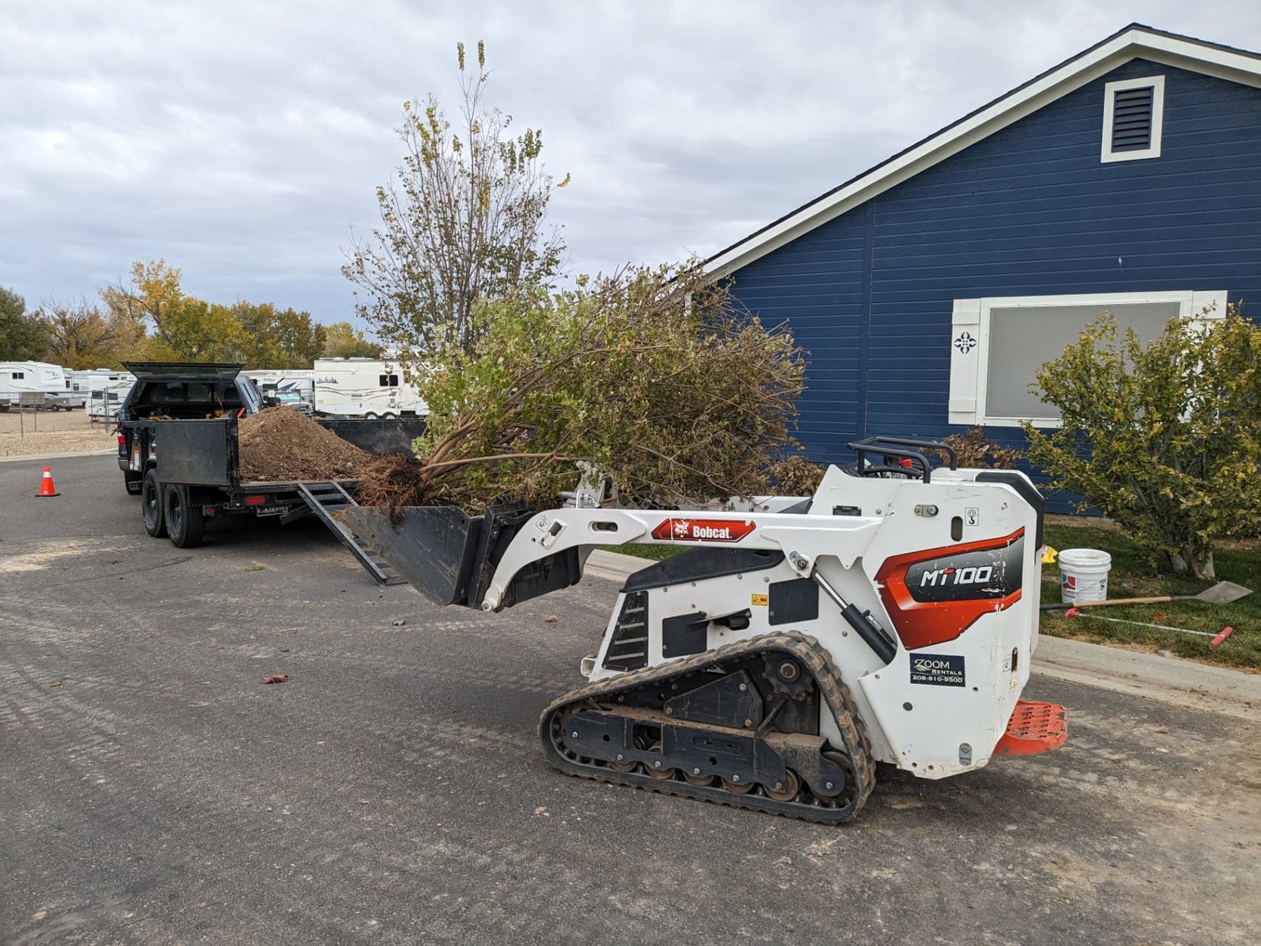 Compact loader moving material beside a work trailer at a residential job